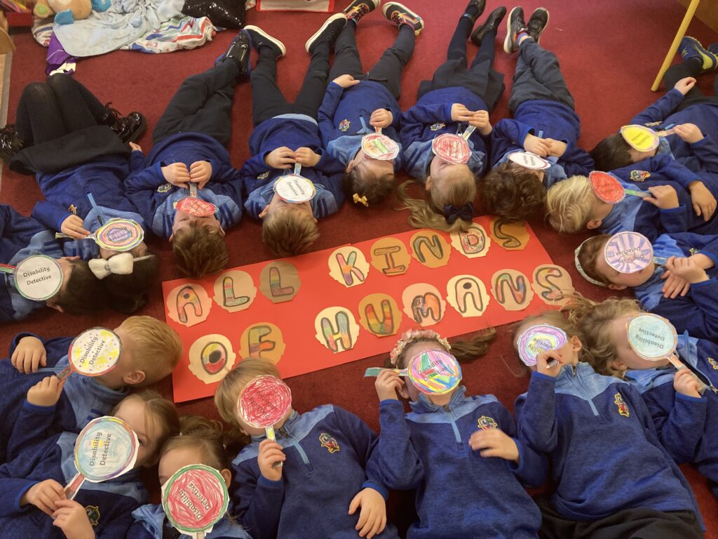 A group of children lying on the floor with a sign, covering their faces with a magnifying glass made of paper