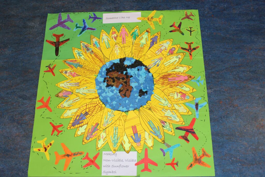 A bright and cheerful poster created by pupils featuring a large sunflower with vibrant yellow petals and a blue and brown center.